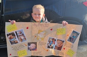 Kenzie (3) holds up a poster titled 'My magic ears' with images of his deaf journey.