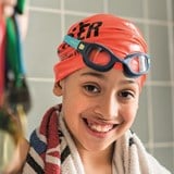 Santiago wearing a swim cap and goggles holding up a bunch of swimming medals.