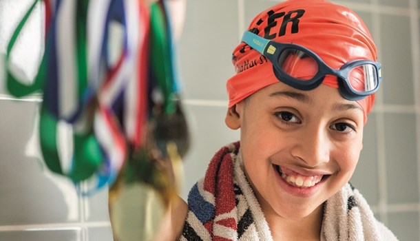 Santiago wearing a swim cap and goggles holding up a bunch of swimming medals.