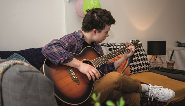 Elliot (22) plays his guitar on his sofa