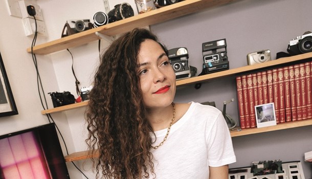 Lily, a photographer, stands in front of a shelf full of cameras