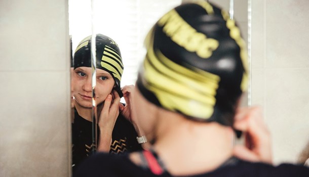 A girl adjusts her hearing technology beneath a swim cap