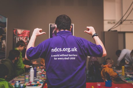 Volunteer pointing to information about the charity on their shirt.