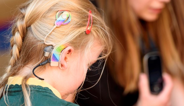 A girl with decorated cochlear implants in front of a woman using a radio aid.
