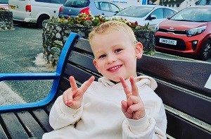 Kenzie (4) sitting on a bench making 'peace' sign with his hands