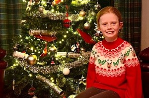 Charlotte (8) sitting in front of a Christmas tree