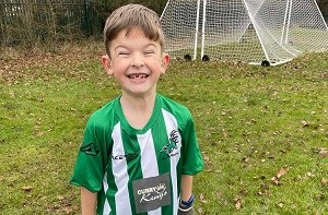 Oliver (8) smiling in his football kit next to a football goal