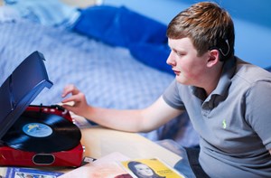 Young man wearing a hearing aid is using a vinyl record player