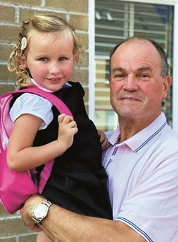 A grandpa holding his deaf granddaughter who is wearing a cochlear implant and pink rucksack.