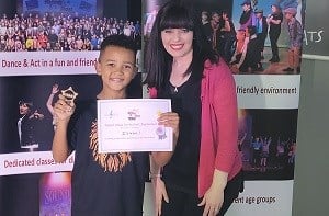 Isaac (8) holding his talent show trophy next to his performing arts teacher 