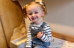 Olivia (2) sitting on a dresser with overall on