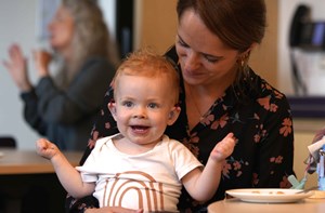 Woman in a cafe holding a happy baby who is wearing hearing 