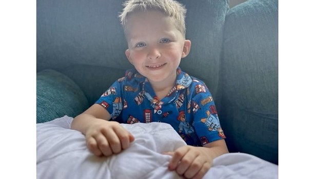 William (5) sits under a blanket on a sofa, smiling at the camera