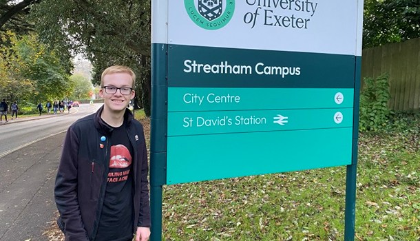 Daniel (18) standing in front of a sign for the University of Exeter