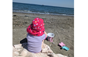 Elina (2) sitting at the beach wearing a sun hat. She faces away from the camera.