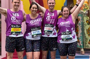 Four smiling adults, dressed in purple vests and matching shorts have their arms raised above their heads