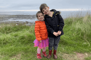 Young boy standing with his sister on a coastline