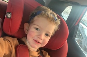 A boy wearing bone conduction hearing aids sitting in a car seat