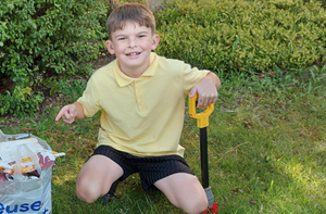 Boy holding a litter picker kneels next to bag full of litter