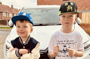 Two young boys standing in front of a parked car